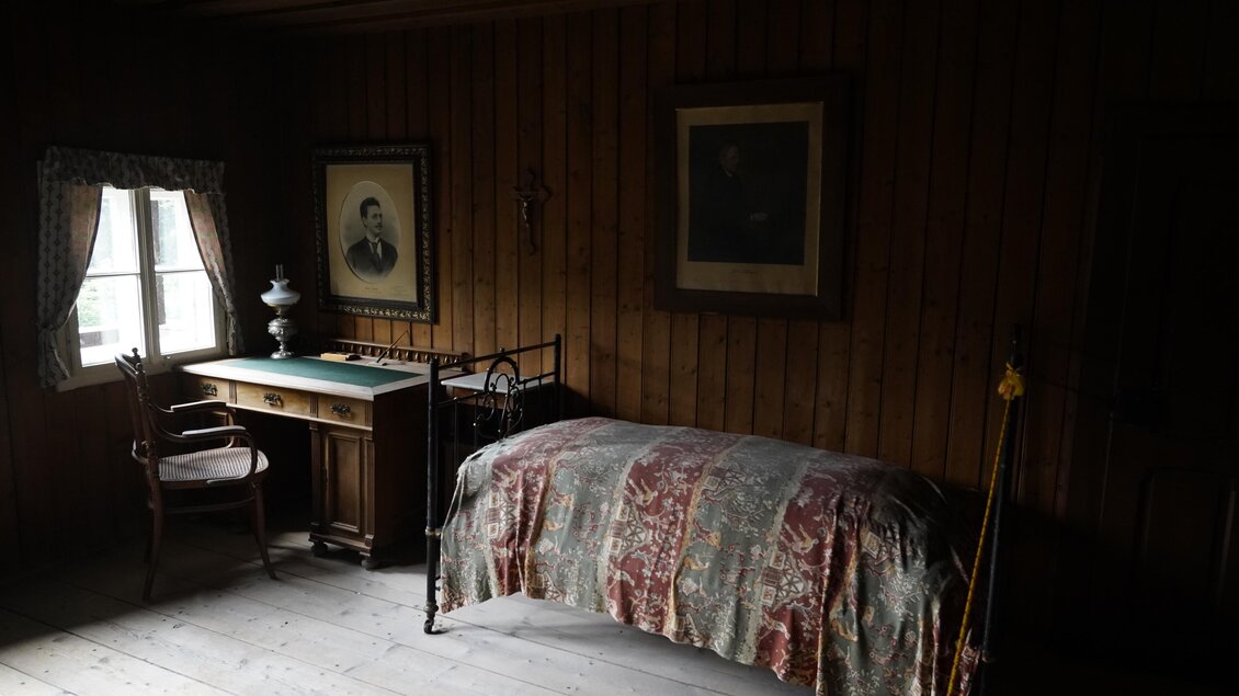 Ein gemütlicher Raum mit einem Bett und einem Schreibtisch aus Holz. Die Wände sind mit Holz verkleidet und es hängen zwei Bilder. | © TV Hochsteiermark/Amelie Kertelits