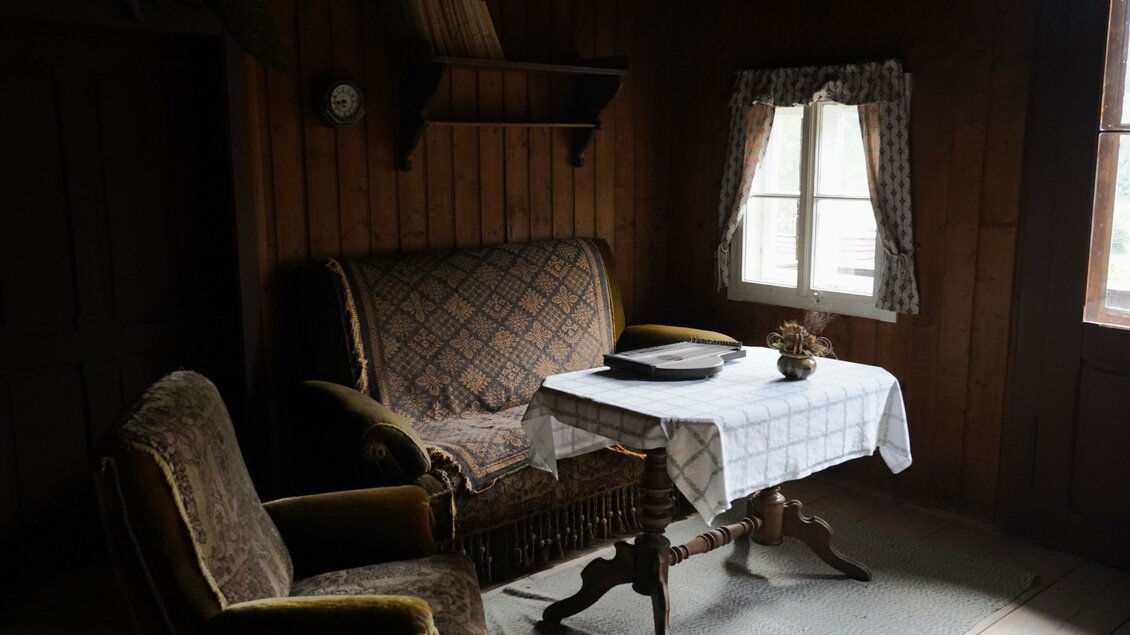 Ein gemütliches Zimmer mit einer alten Couch und einem Tisch. Das Licht fällt durch ein Fenster auf die Tischdecke. | © TV Hochsteiermark/Amelie Kertelits