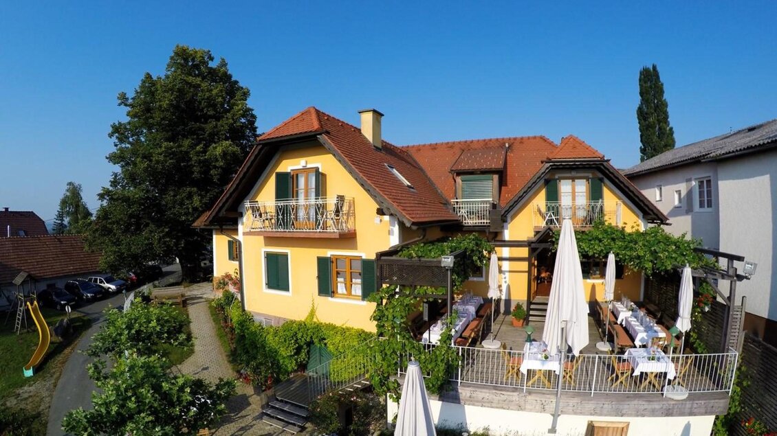 Ein charmantes gelbes Haus mit einem Balkon und weißen Sonnenschirmen. Der Garten ist grün und einladend, ideal für entspannte Stunden im Freien. | © Das Restaurant_