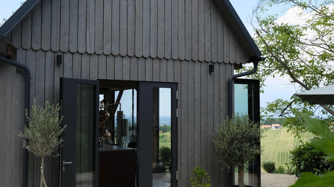 Ein modernes Holzhaus mit großen Fenstern und einem einladenden Eingangsbereich. Umgeben von kleinen Pflanzen und Kieswegen. | © STIN OG