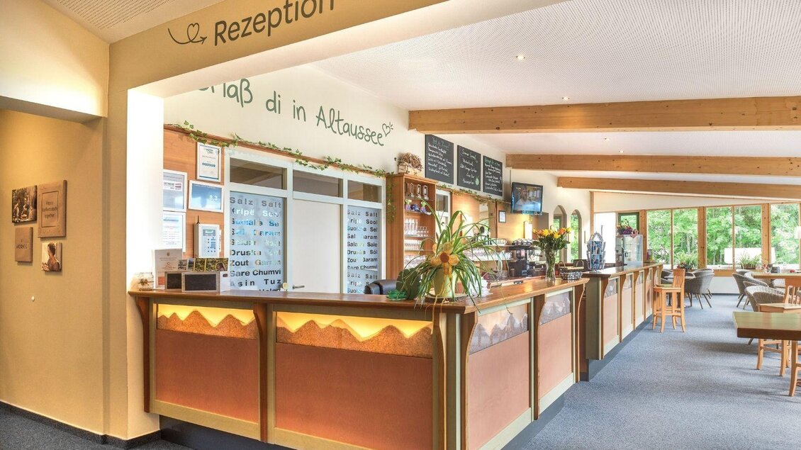 Ein Empfangsbereich mit einer hellen, einladenden Theke und Pflanzen. Im Hintergrund sind große Fenster, die viel Licht hereinlassen. | © JUFA Hotels