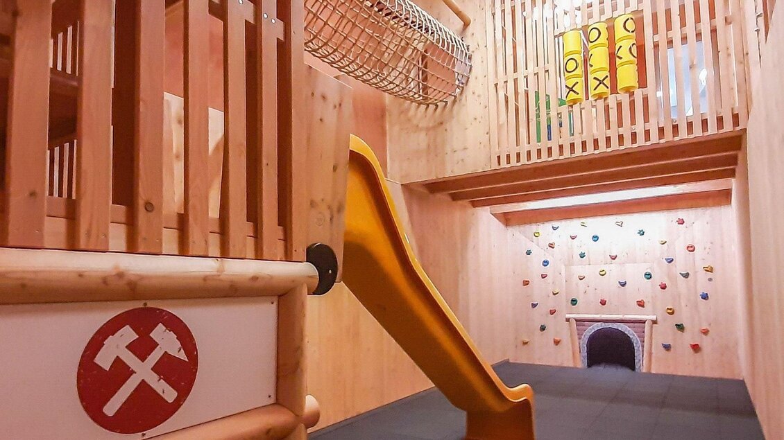 Ein Spielbereich mit Rutsche und Kletterwand. Der Raum hat helle Holzverkleidung und ist kinderfreundlich gestaltet. | © JUFA Hotels