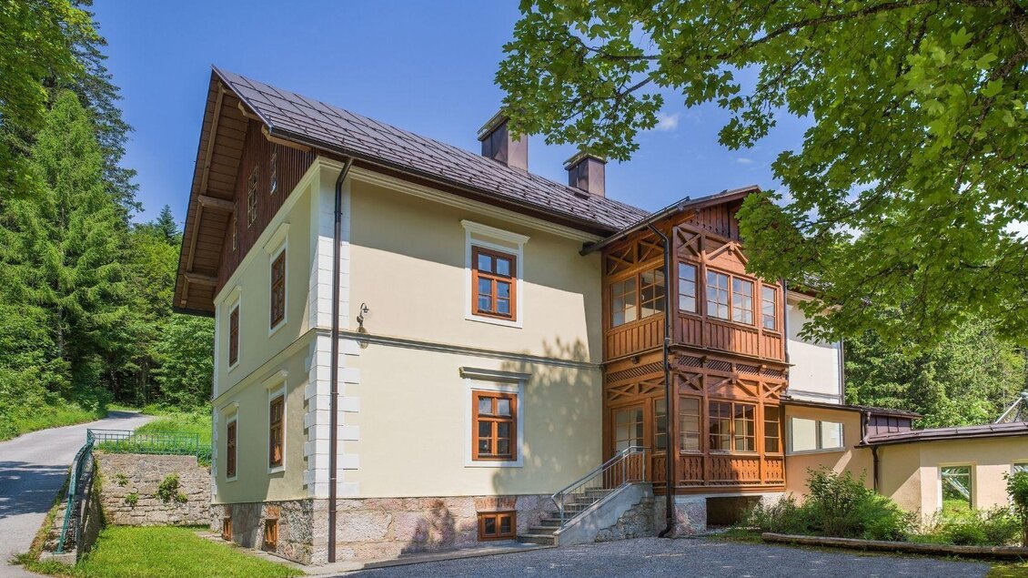 Ein schönes Haus im modernen Landhausstil, umgeben von bewaldeter Landschaft. Die Fassade ist hell mit großen Fenstern und einem verglasten Erker. | © JUFA Hotels