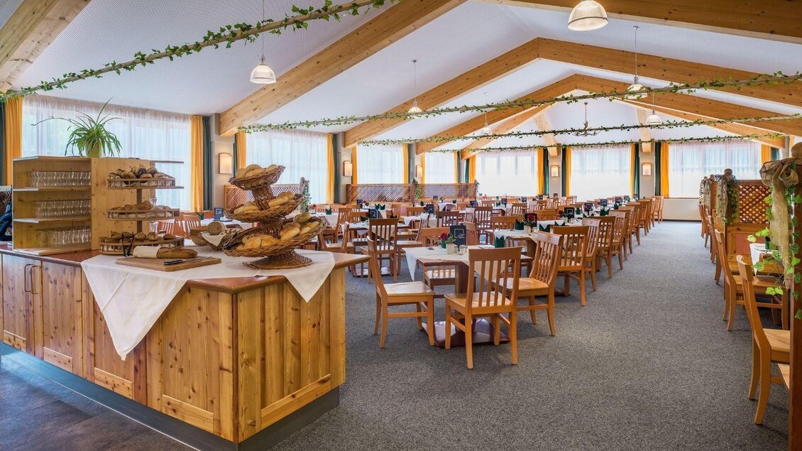 Ein einladendes Restaurant mit Holzelementen und einer gemütlichen Atmosphäre. Die Tische sind ordentlich gedeckt und das Licht strömt durch große Fenster. | © JUFA Hotels