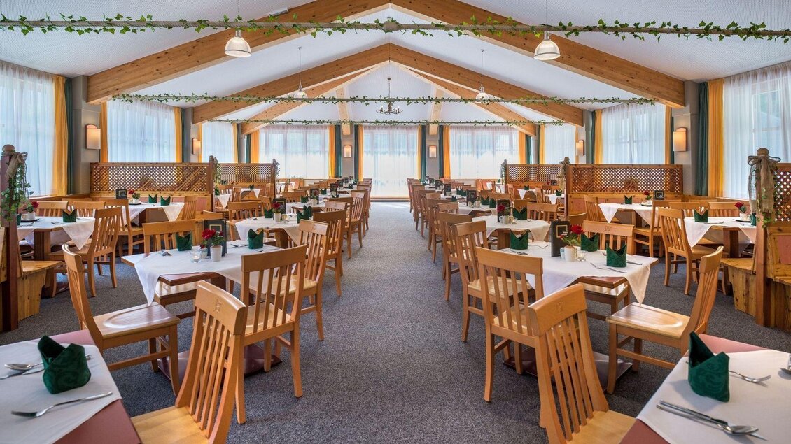 Ein einladendes Restaurant mit Holztischen und Stühlen. Die Beleuchtung ist warm und die Fenster lassen viel Tageslicht herein. | © JUFA Hotels