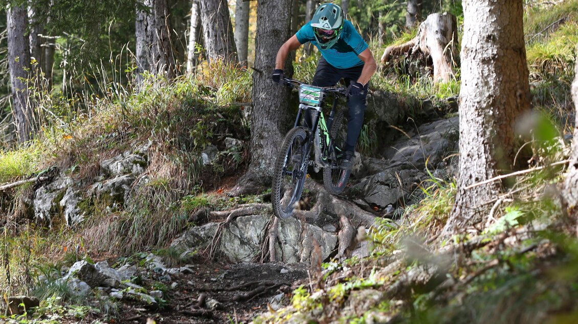 Mountainbiker mit Helm fährt über Felsen und Wurzeln auf einem Waldtrail am Schöckl bergab. | © The Gap MTBing