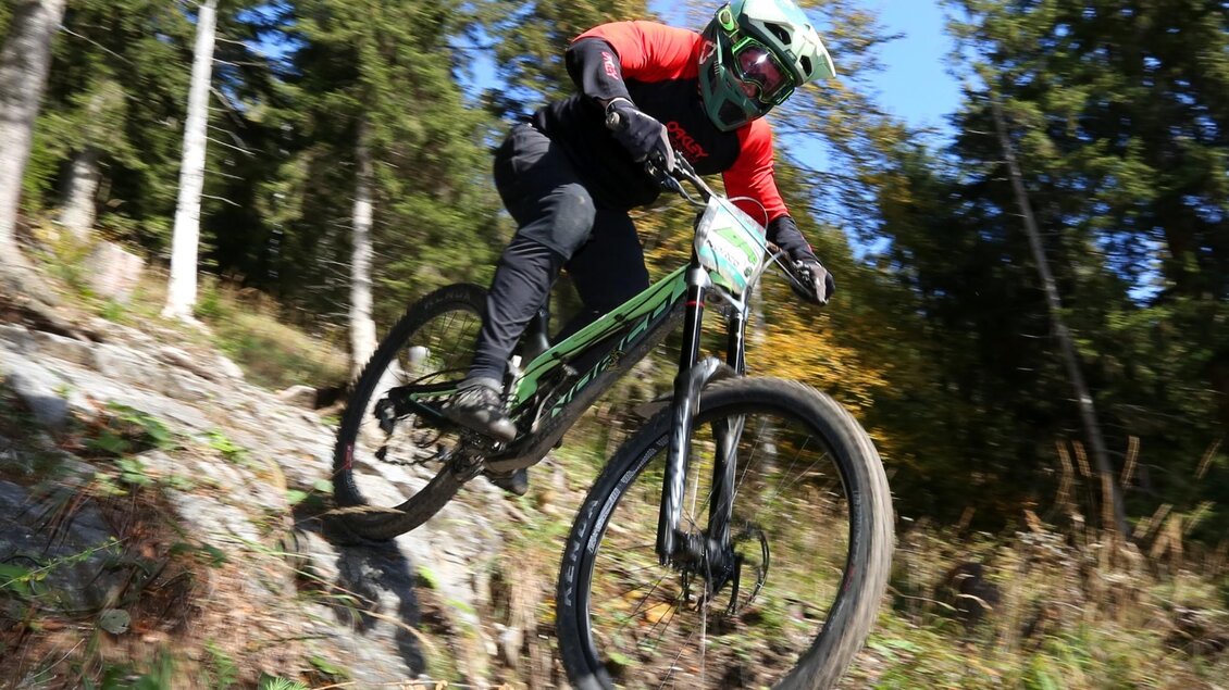 Mountainbiker mit Helm fährt auf einem felsigen Schöckl Trail durch den Wald bergab. | © The Gap MTBing