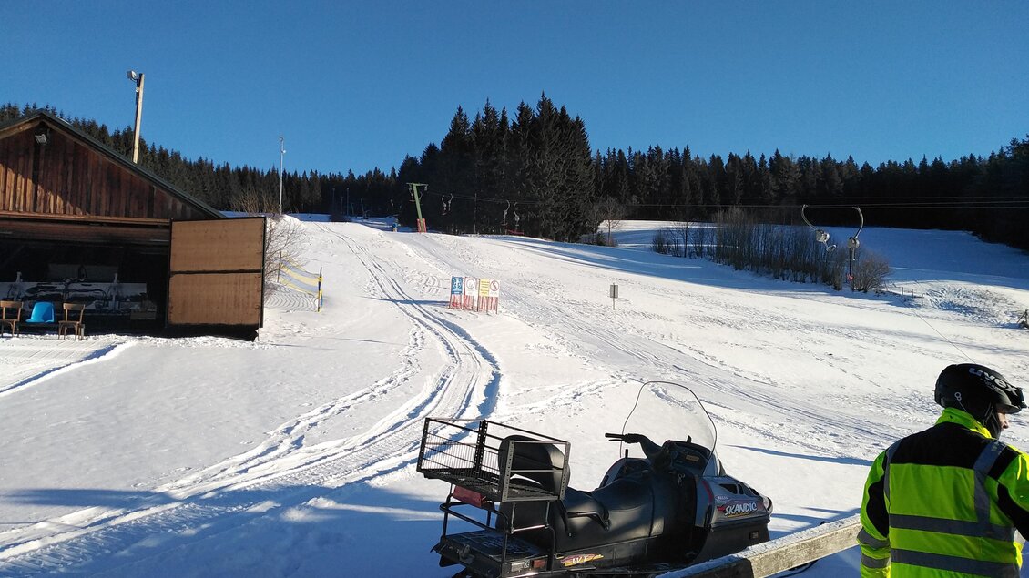 Ein Arbeiter mit Skidoo auf einer Skipiste und einer Holzhütte im Hintergrund.Mit strahlend blauem Himmel. | © Harald Kaiser