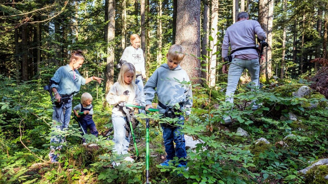 Eine Gruppe von Kindern und Erwachsenen arbeitet gemeinsam im Wald. Sie sind umgeben von Bäumen und Sträuchern und benutzen Geräte für die Outdoor-Aktivität. | © www.zloam.at