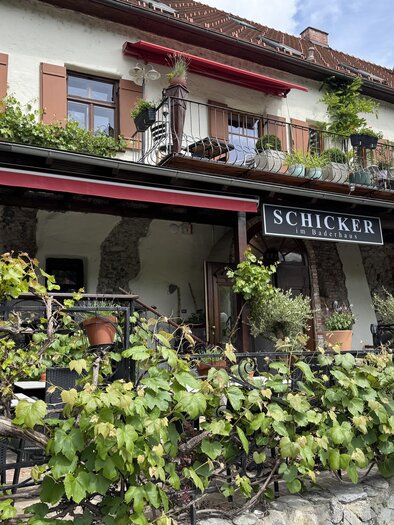 A charming restaurant with a balcony and many plants. The facade is surrounded by lush greenery, creating an inviting atmosphere. | © TV Hochsteiermark
