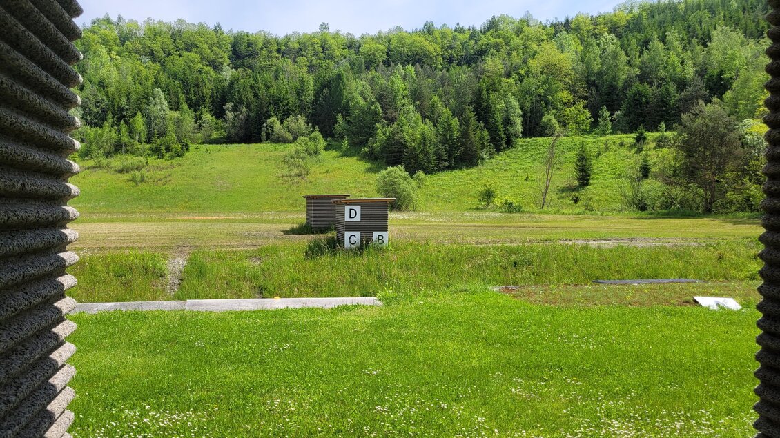 Blick aus einem überdachten Schießstand auf Zielscheibe, Wiese und bewaldeten Hang in der Schießarena Zangtal  | © TV Region Graz