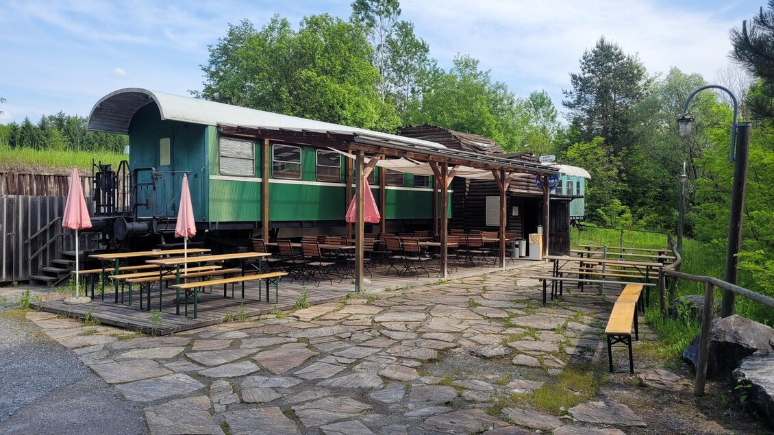 Café in einem grünen Eisenbahnwaggon mit überdachtem Gastgarten und Sitzbänken in der Schießarena Zangtal in Voitsberg  | © TV Region Graz