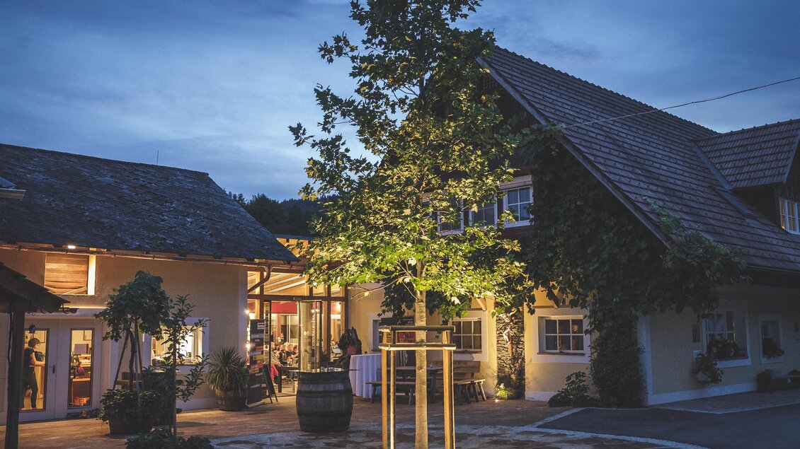 Ein charmantes Gasthaus bei Dämmerung mit warmem Licht und einem schönen Baum im Innenhof. Die Atmosphäre ist einladend und gemütlich. | © Schilcherei Jöbstl