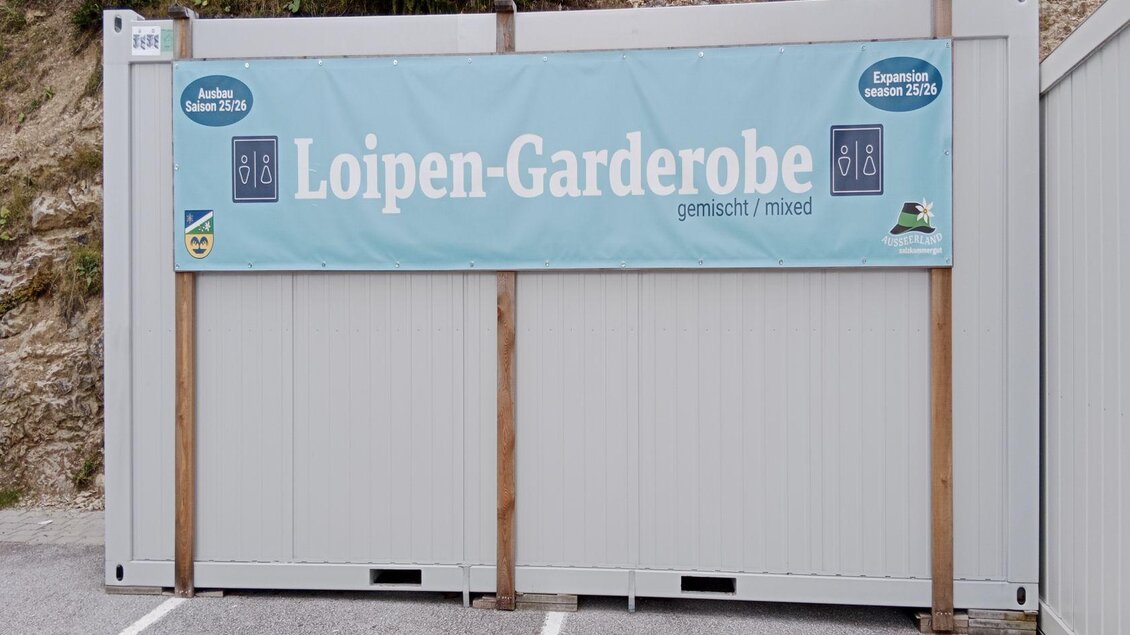 <p>Ein Bereich mit einem blauen Banner, das die "Loipen-Garderobe" anzeigt. Diese Umkleide steht am Parkplatz der Tauplitzalm.</p> | © TVB Ausseerland Salzkammergut_(c)Kolb