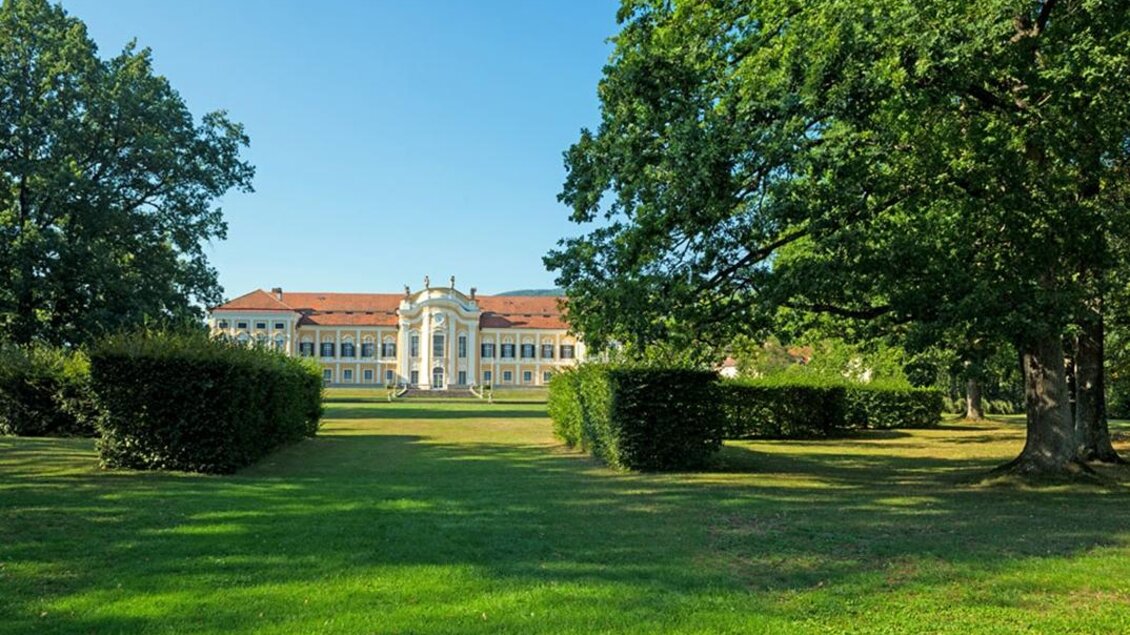 Ein prächtiges Schloss umgeben von grünem Rasen und großen Bäumen. Der Himmel ist klar und blau. | © Schloss Schielleiten