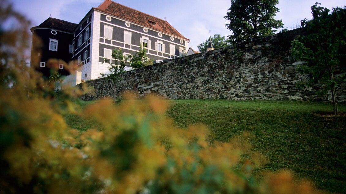 Ein historisches Gebäude mit einem steinernen Wall und grüner Wiese im Vordergrund. Im Hintergrund sind Bäume und ein klarer Himmel sichtbar. | © Schlösserstraße