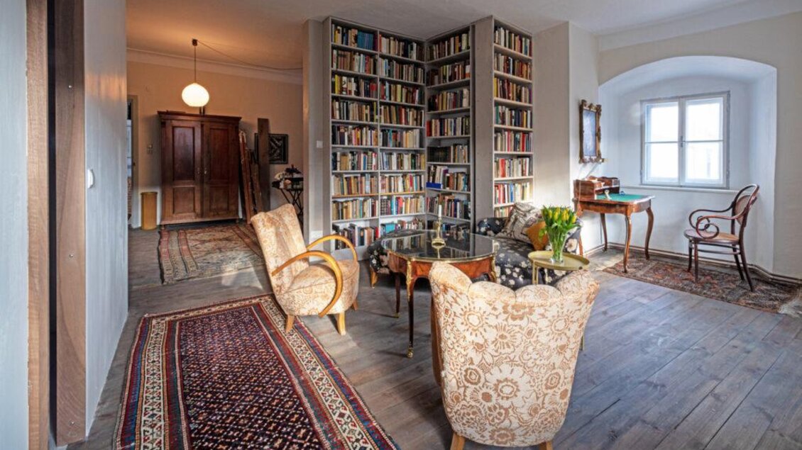 Ein gemütlicher Raum mit einem Bücherregal und einem runden Tisch. Bequeme Stühle und ein dekorativer Teppich verleihen dem Raum einen einladenden Charakter. | © Grill