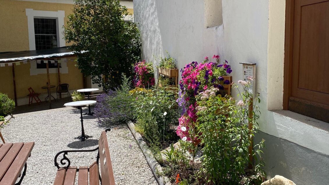 Ein schöner Gartenbereich mit bunten Blumen und einer Kiesfläche. Zwei Holzbänke laden zum Verweilen ein. | © Naturpark Sölktäler - Julia Aigner