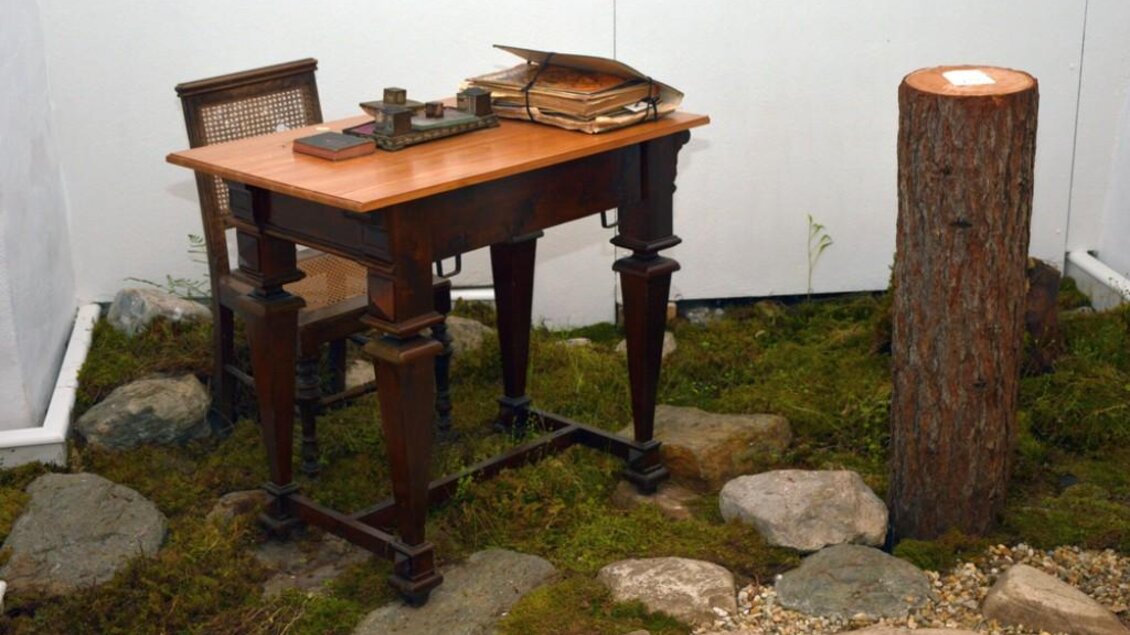 Ein Holztisch steht auf moosbedecktem Boden, umgeben von Steinen. Auf dem Tisch liegen einige Bücher und Schreibutensilien. | © Naturpark Sölktäler