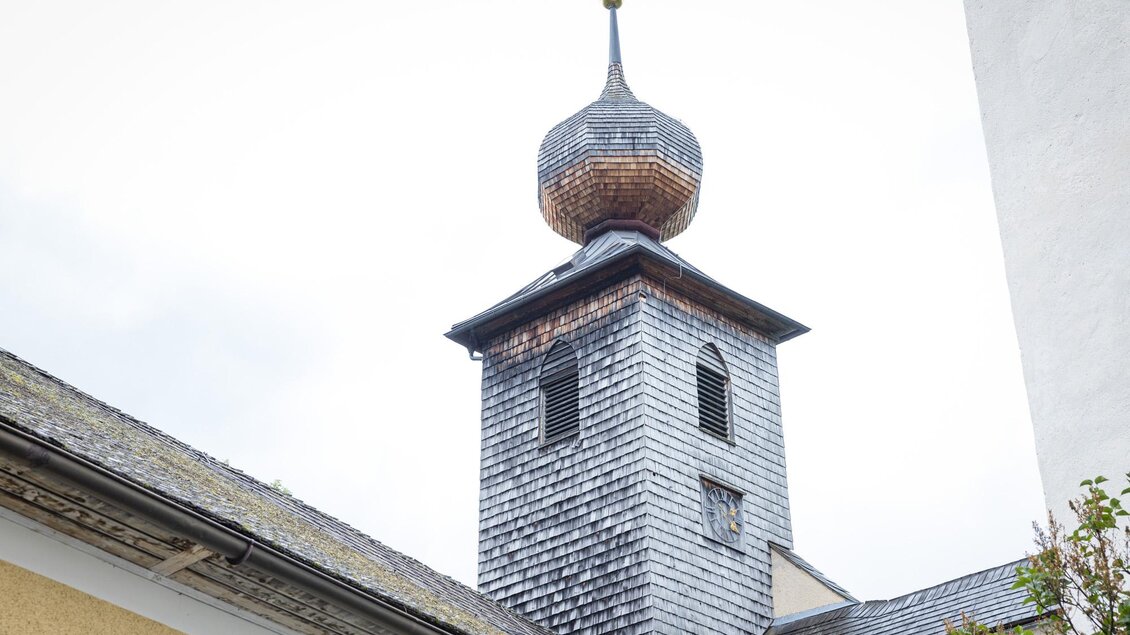 Ein Kirchturm mit einer charakteristischen zwiebelförmigen Kuppel. Die Fassade ist aus Holzschindeln und liegt in einer ruhigen Umgebung. | © wildbild