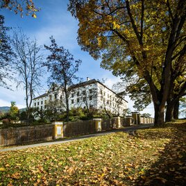 A historic building surrounded by colorful autumn leaves. The sun shines through the trees, creating a picturesque atmosphere. | © TVB Murau