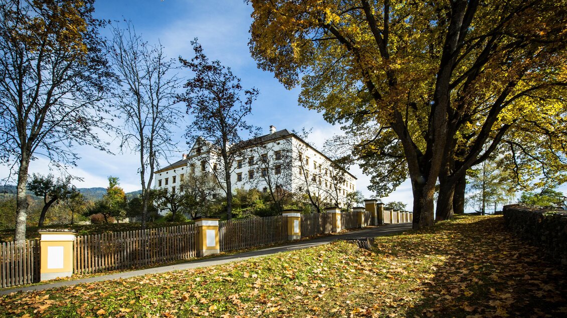 Ein historisches Gebäude umgeben von buntem Herbstlaub. Die Sonne scheint durch die Bäume und sorgt für eine malerische Atmosphäre. | © TVB Murau