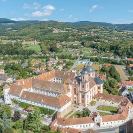 A picturesque view of a monastery with beautiful buildings and a landscape in the background. The surroundings consist of forests and small villages. | © Helmut Schweighofer