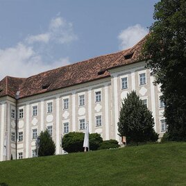 An impressive building with a white facade and red roofs. The castle is situated on a hill, surrounded by trees and green spaces. | © Enrico Caracciolo