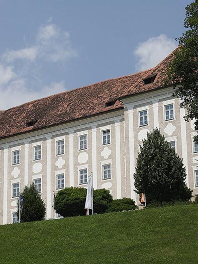 Ein imposantes Gebäude mit einer weißen Fassade und roten Dächern. Das Schloss liegt auf einem Hügel, umgeben von Bäumen und Grünflächen. | © Enrico Caracciolo