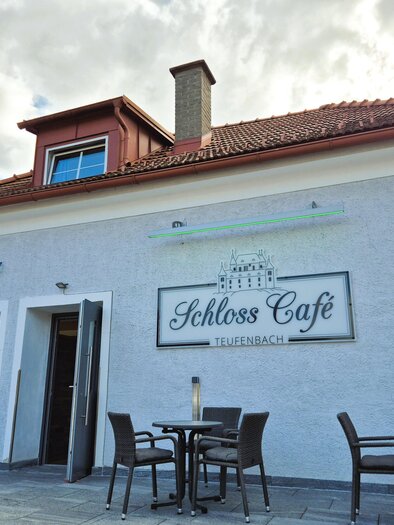 Ein einladendes Café mit dem Namen "Schloss Café" in Teufenbach. Die Fassade ist hell gestrichen und es stehen Tische draußen bereit. | © TV Murau