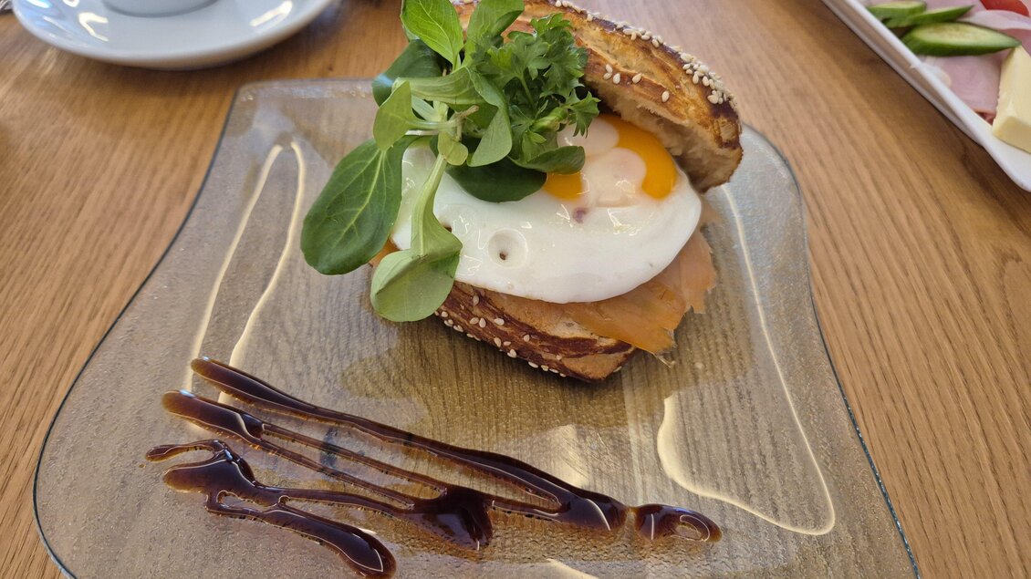 Ein belegtes Brötchen mit einem Spiegelei, Schinken und frischem Salat. Dazu ist eine dunkle Sauce auf dem Teller angerichtet. | © TV Murau