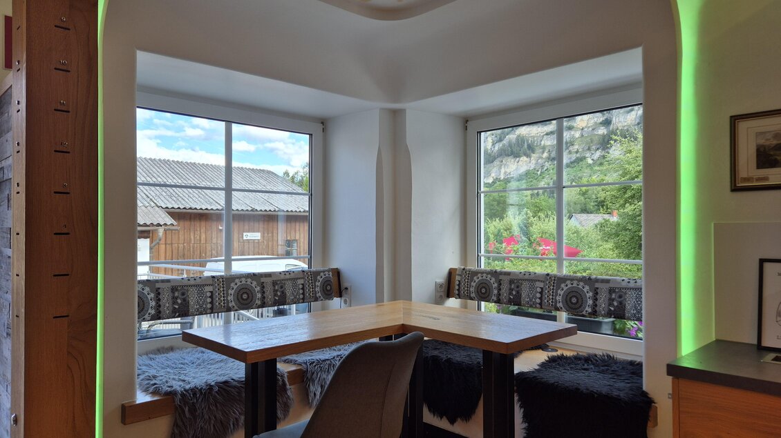 Eine gemütliche Sitzecke mit Fensterblick auf die Natur. Der Tisch ist gut beleuchtet und die Bänke sind mit Decken dekoriert. | © TV Murau