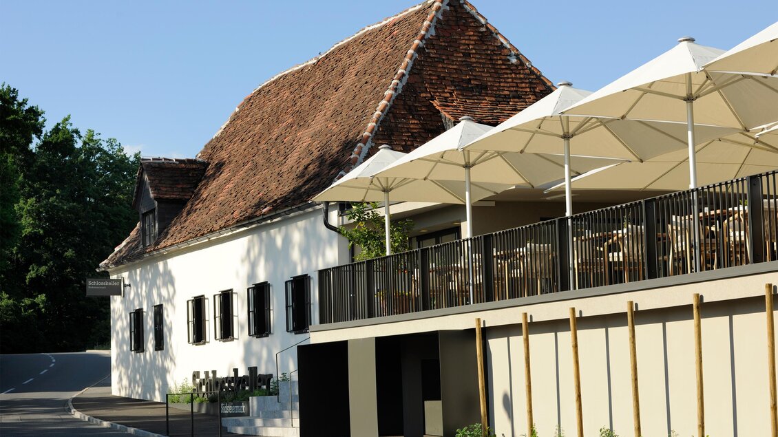Ein charmantes Gebäude mit einem Reetdach und modernen Terrassendächern. Die sonnige Atmosphäre lädt zum Verweilen ein. | © Schlosskeller Südsteiermark