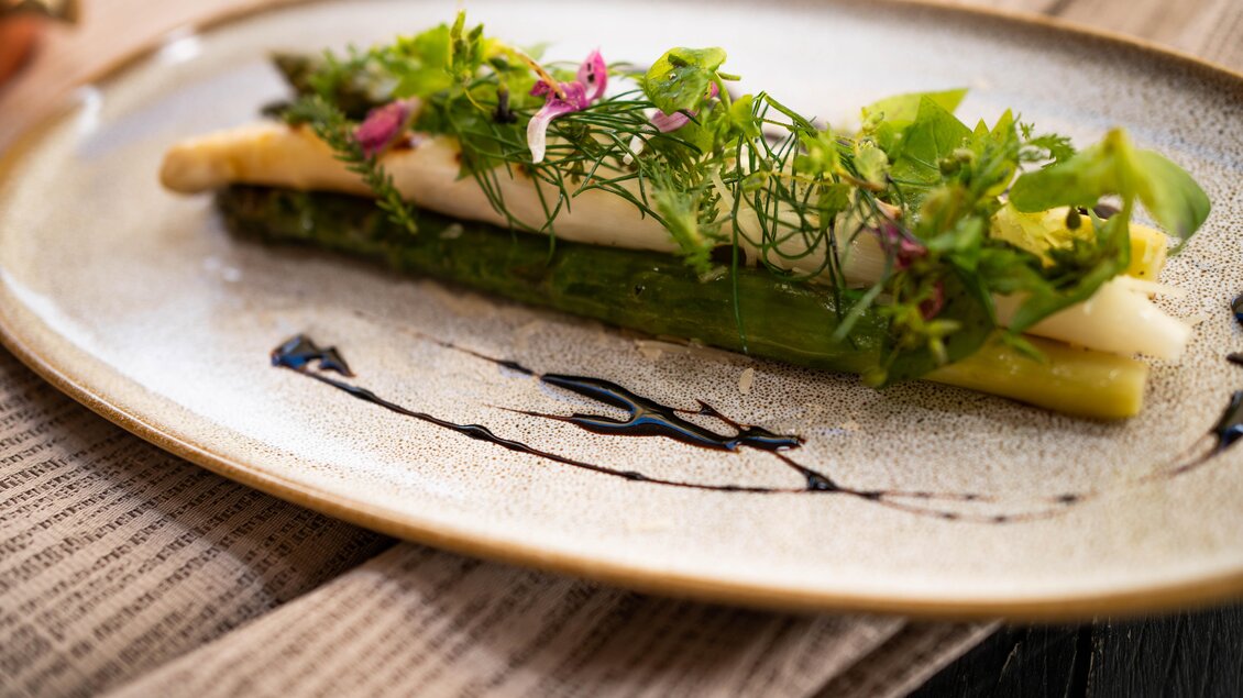 Ein kunstvoll angerichteter Teller mit grünem Spargel und frischen Kräutern. Die Kombination wird von einer feinen Sauce begleitet. | © Schlosskeller Südsteiermark