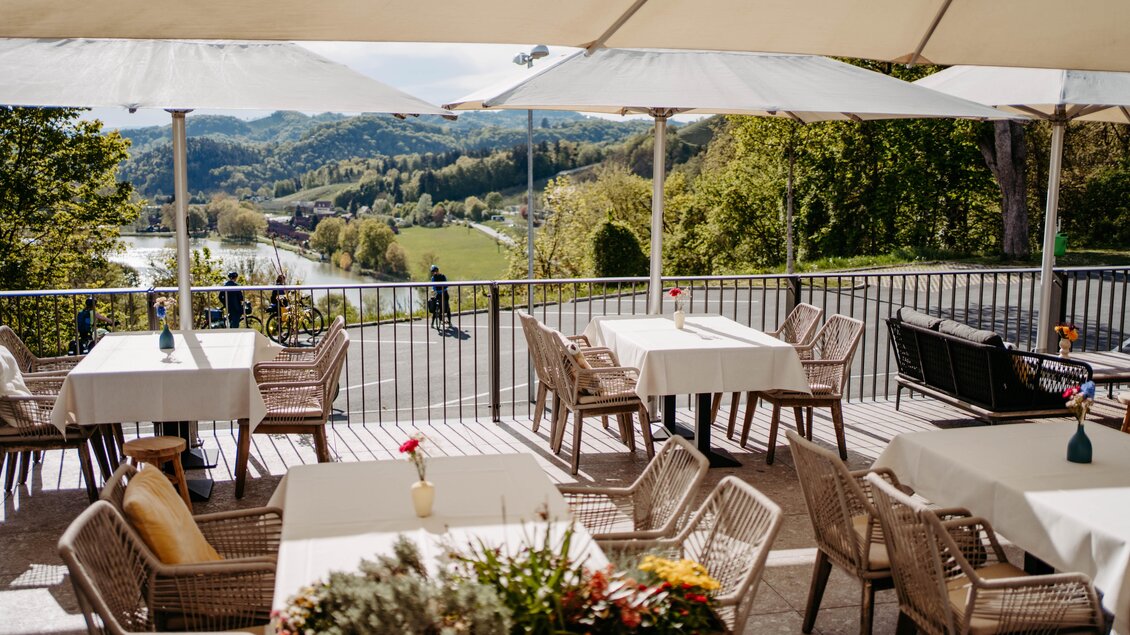 Eine gemütliche Terrasse mit Tischen und Stühlen, umgeben von Bäumen und einer Aussicht auf die Natur. Der Himmel ist klar und die Atmosphäre ist einladend. | © Schlosskeller Südsteiermark