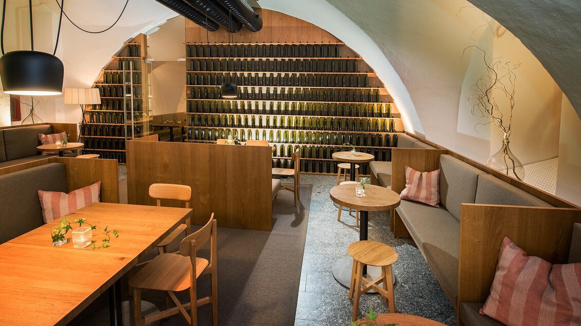 Ein modernes Restaurant mit Holzinterieur und gemütlichen Sitzbereichen. An den Wänden sind Weinregale zu sehen, die eine einladende Atmosphäre schaffen. | © Stefan Kristoferitsch