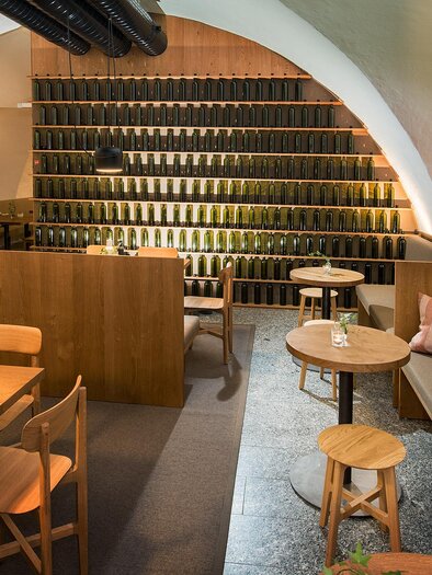 Ein modernes Restaurant mit Holzinterieur und gemütlichen Sitzbereichen. An den Wänden sind Weinregale zu sehen, die eine einladende Atmosphäre schaffen. | © Stefan Kristoferitsch