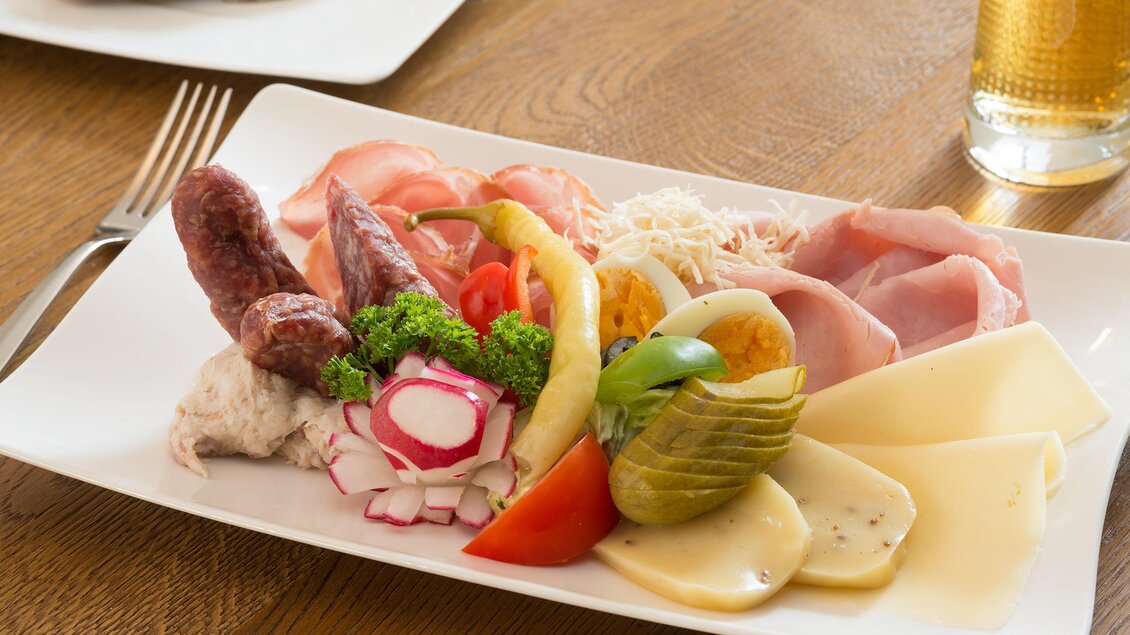 Ein Teller mit verschiedenen Wurst- und Käsesorten, frischem Gemüse und hartgekochtem Ei. Der Hintergrund zeigt Holz und ein Getränk. | © Stefan Kristoferitsch