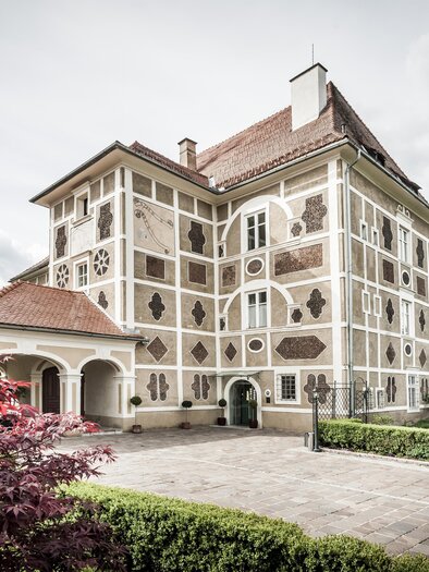 Ein elegantes Gebäude mit einzigartiger Fassadengestaltung. Umgeben von Grün und Blumen wirkt es einladend und charmant. | © Schloss Farrach