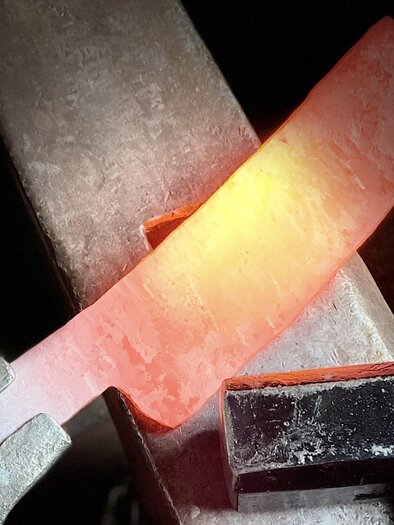 Ein glühendes Metallstück wird bearbeitet. Werkzeug und Anvil sind im Vordergrund sichtbar. | © Kurt Forstner