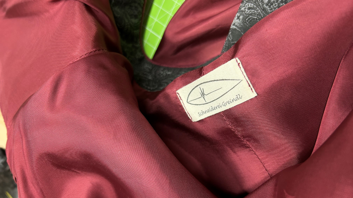 Eine rote Bekleidungsstück mit einer grauen Innenfutter. Ein Etikett mit dem Namen der Marke ist sichtbar. | © Maria Greindl