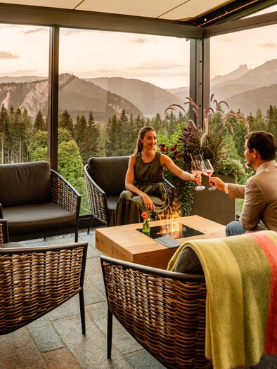 A cozy terrace with a fire pit and a view of the mountains. A couple enjoys an evening with drinks and a beautiful view. | © Christine Höflehner