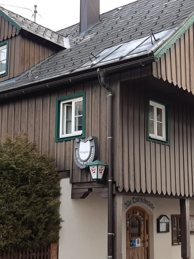 Ein traditionelles Holzhaus mit einem breiten Dach und grünen Fensterrahmen. Vor dem Haus befindet sich eine kleine Hecke und ein Schild mit dem Namen des Hauses. | © TVB Ausseerland Salzkammergut_Daniela Casari