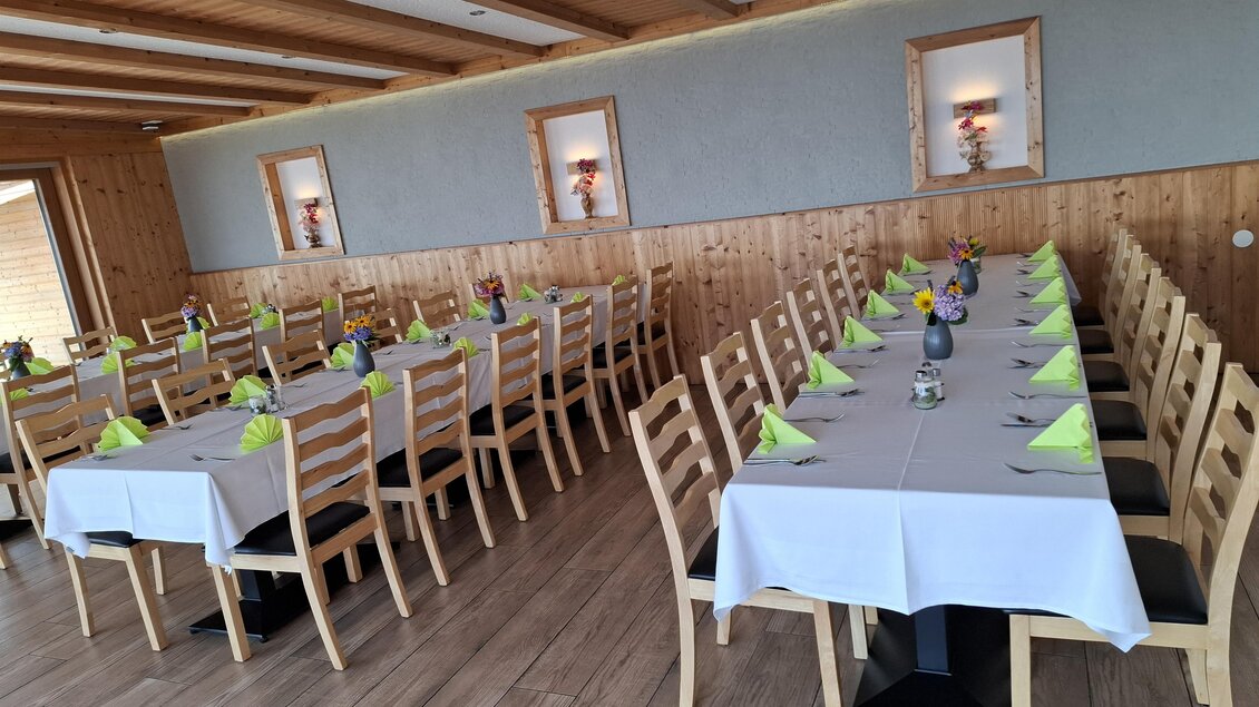 Ein eleganter Speisesaal mit langen Tischen und Holzverkleidung. Die Tische sind mit weißen Tischdecken und grünen Servietten dekoriert. | © Mesnerhaus
