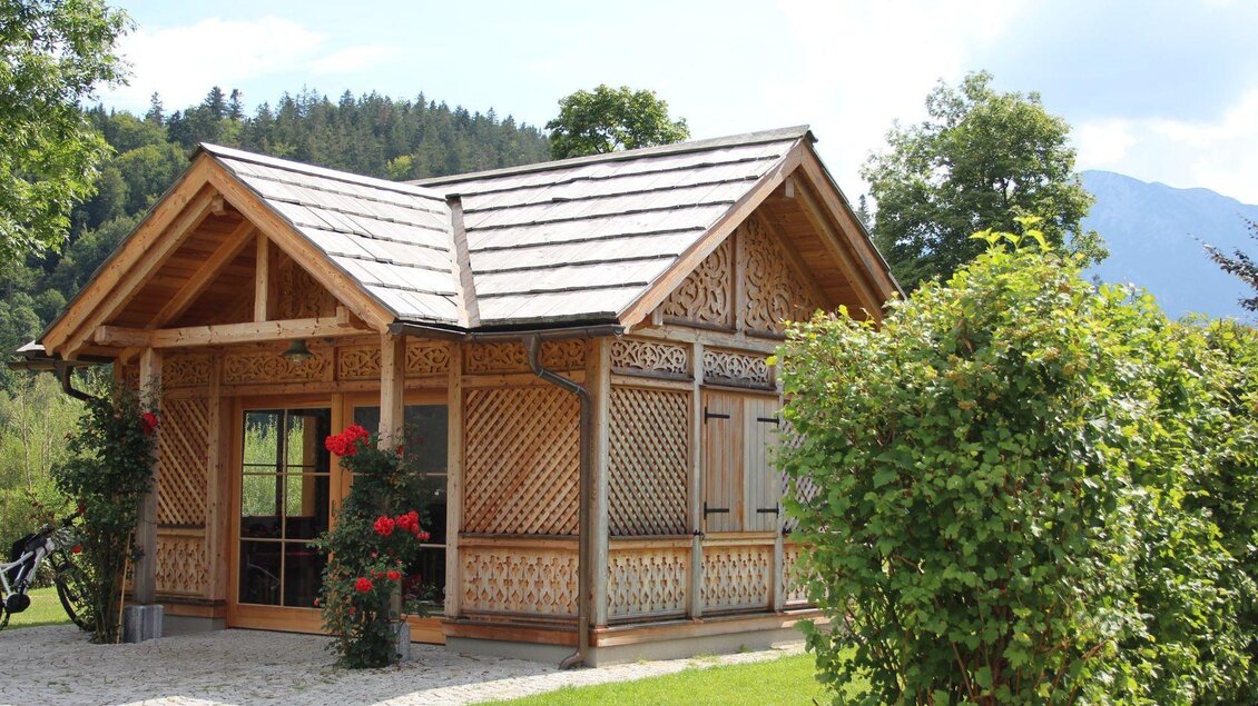 Ein charmantes Holzhaus mit kunstvollen Verzierungen und einem gepflegten Garten. Umgeben von grünen Bäumen und einer idyllischen Landschaft. | © Viola Lechner