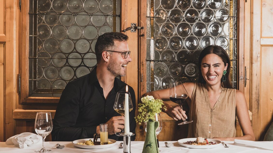 Ein Paar sitzt an einem elegant gedeckten Tisch in einem Restaurant. Sie lachen und genießen ihre Mahlzeit bei Kerzenlicht. | © Seehotel Jägerwirt