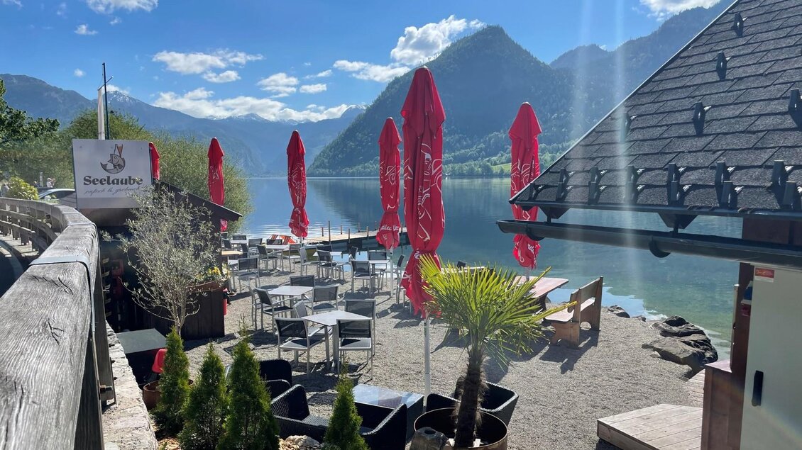 Ein idyllischer See mit einem Restaurant am Ufer. Rote Sonnenschirme und Tische laden zum Verweilen ein, umgeben von Bergen und Bäumen. | © TVB Ausseerland/Bettina Scheck