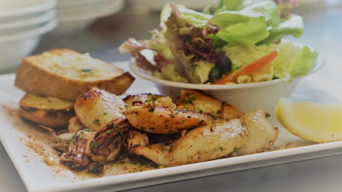 Ein Teller mit gegrillten Meeresfrüchten, knusprigem Brot und einem frischen Salat. Dazu ein Stück Zitrone für den Geschmack. | © Seerestaurant Gruber