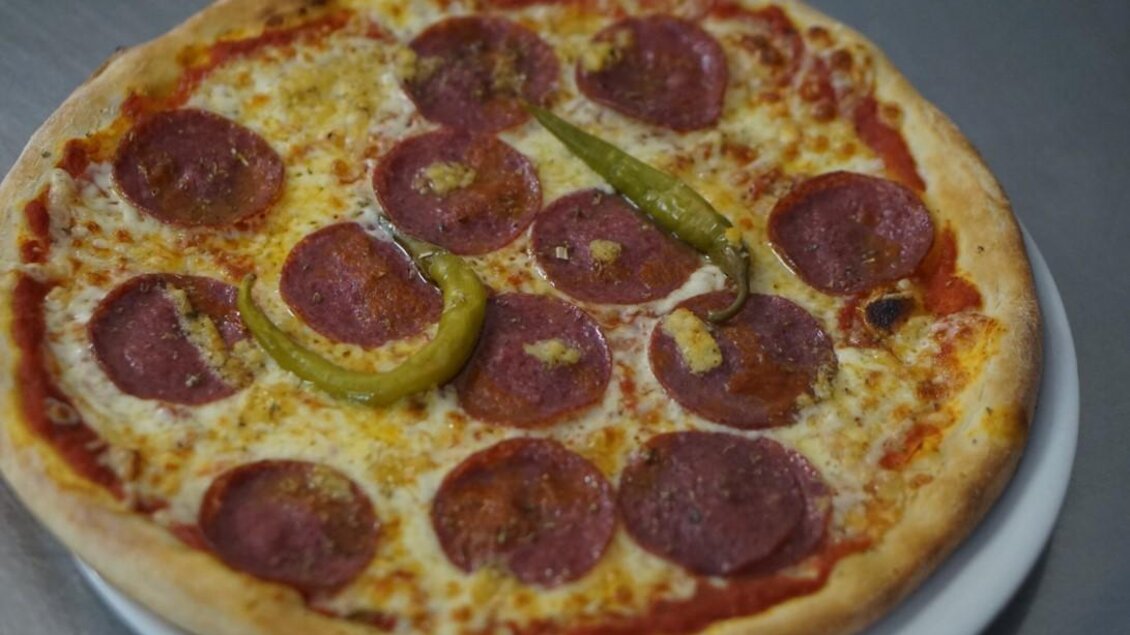 Eine Pizza mit Salami, Käse und grünen Peperoni. Der Teig ist goldbraun und knusprig. | © Seerestaurant Gruber