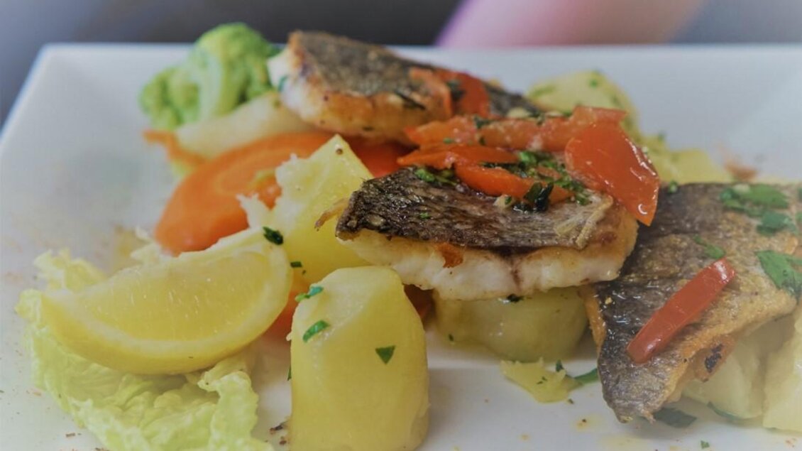 Ein schön angerichteter Teller mit gebratenem Fisch, Kartoffeln und buntem Gemüse. Frische Zitronenscheiben und Kräuter runden das Gericht ab. | © Seerestaurant Gruber